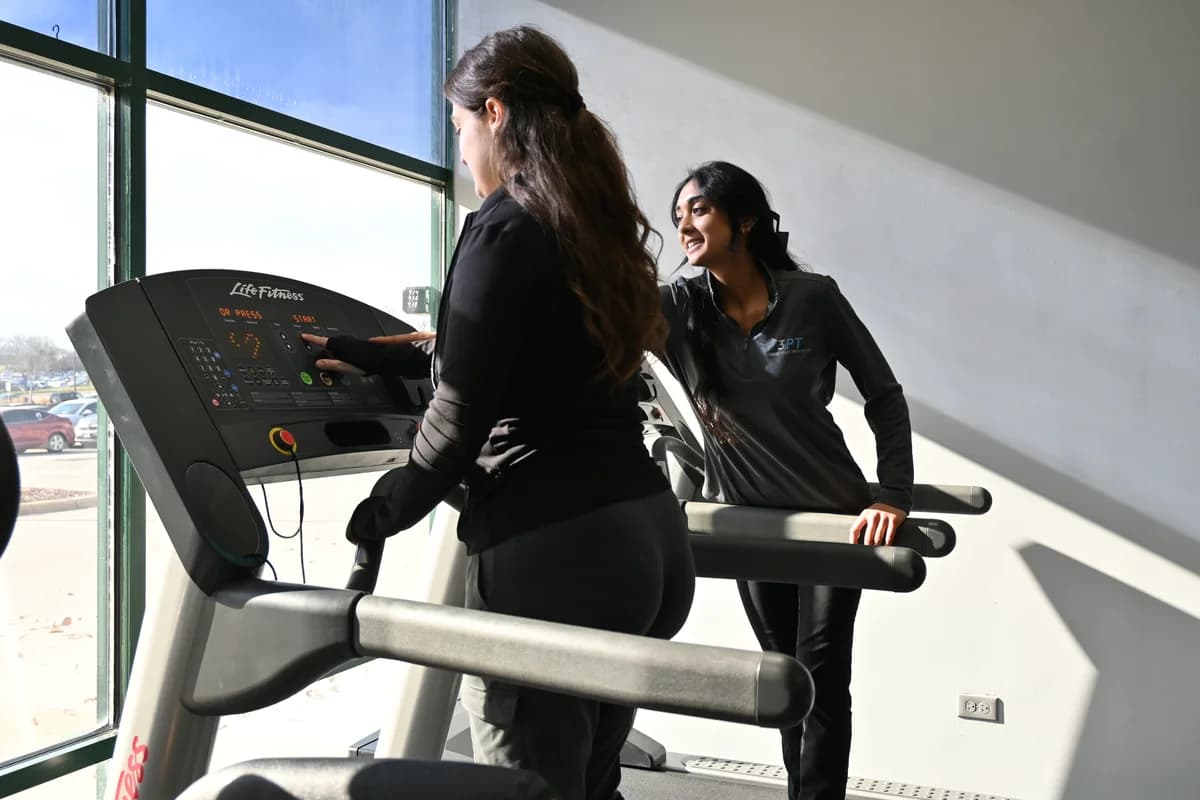 A 3PT physical therapist coaching a patient through a supervised treadmill session at a Three Point Healthcare clinic.
