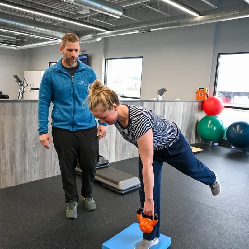 A 3PT Joliet physical therapist observing a patient perform a single-leg deadlift with a kettlebell.
