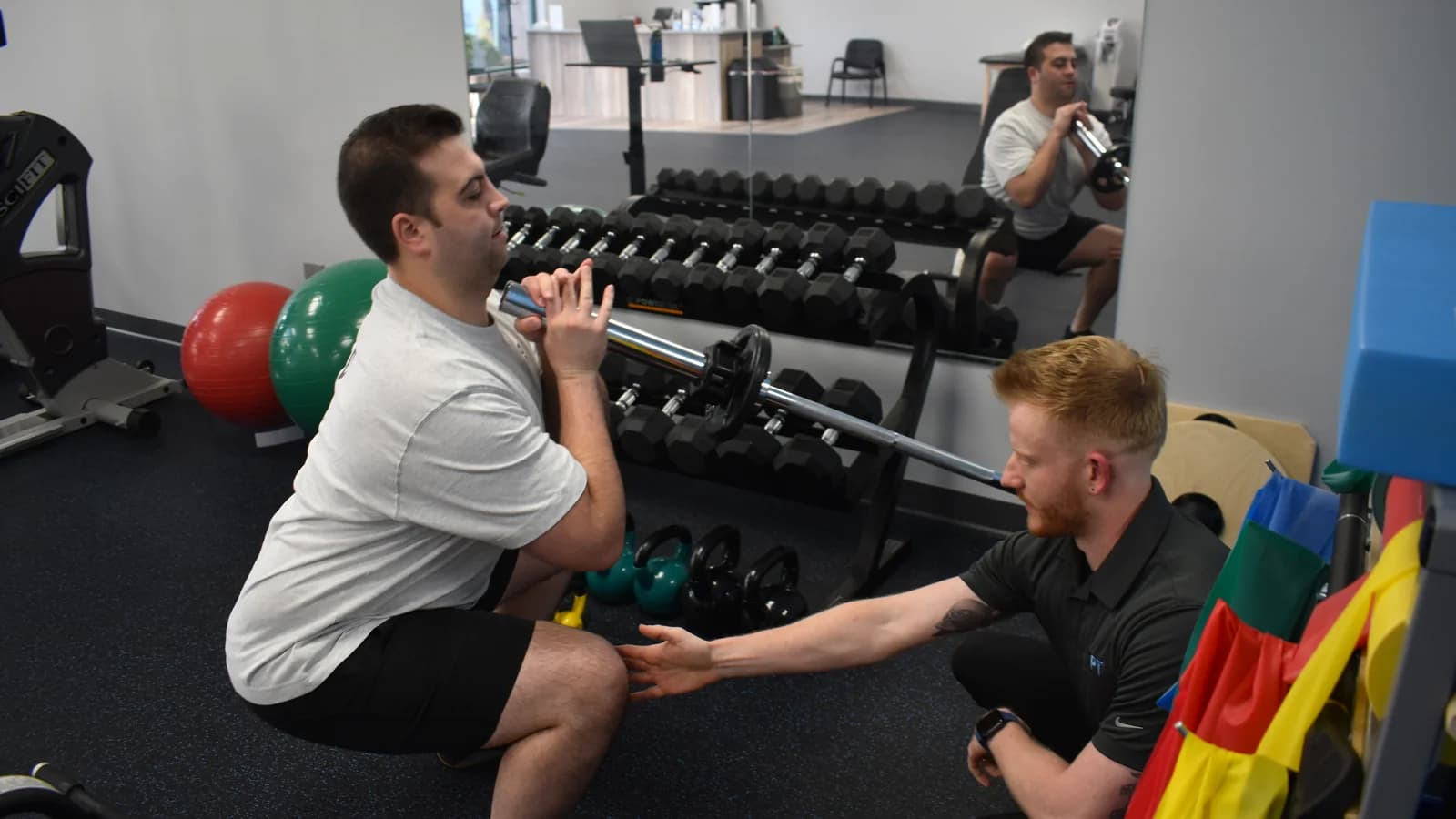 A 3PT Melrose Park physical therapist coaching a patient through a supervised barbell squat at the clinic.